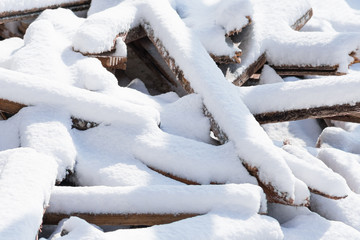Photo of wooden bars and planks, chaotically dumped in a pile, covered with white snow