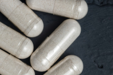 White medical capsules of glucosamine chondroitin, healthy supplement pills on a dark background, macro image