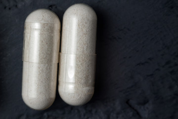 White medical capsules of glucosamine chondroitin, healthy supplement pills on a dark background, macro image