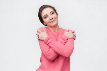 woman l keeping arms around herself, enjoying soft fabric of her pink sweater