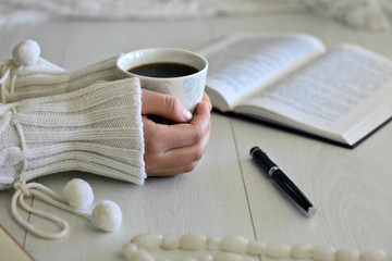 Women's hands, a book and coffee on the table