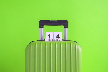 Luggage with valentines day date calendar on green background minimalistic vacation concept.