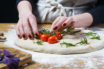 The chef prepares Focaccia, lays tomatoes on the dough. side view, wooden background