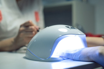 Woman is drying her nails in a UV lamp in a nail salon.