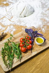 Ingredients for Focaccia: dough, tomatoes, rosemary, thyme, Basil, olive oil on a wooden table. Side view, wooden background