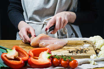 The chef cuts chicken Breasts on a wooden chopping Board. Background kitchen, side view