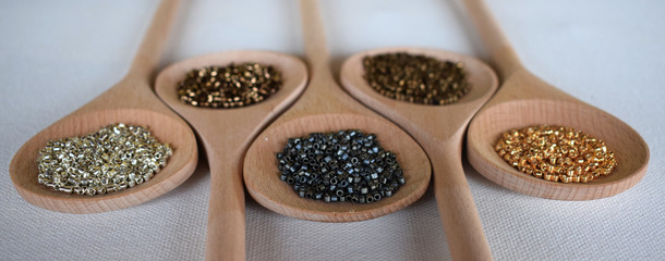 Wooden spoons full of seed beads on a white background