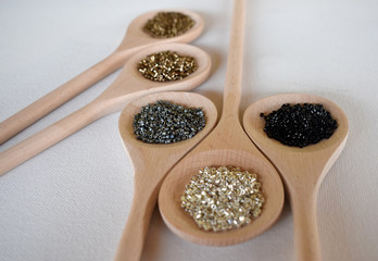 Wooden spoons full of seed beads on a white background