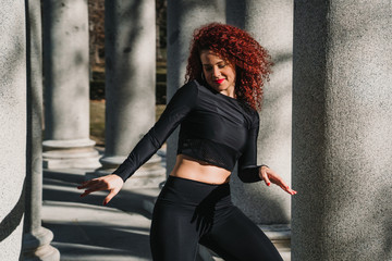 .Young and attractive red haired latin woman dancing urban style on the street .between stone columns on a sunny winter day. Wear sports clothes Positive attitude, happiness. Lifestyle.