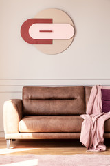Pink blanket on leather couch in modern living room interior with poster on white wall. Real photo