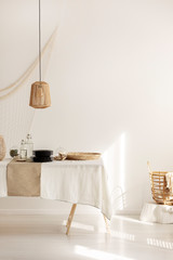 Rattan lamp above dining table with wicker pater and plates, copy space on empty white wall