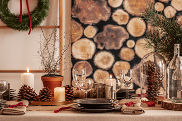 Dining room table set for christmas, wine glasses, cones and black plates on linen tablecloth