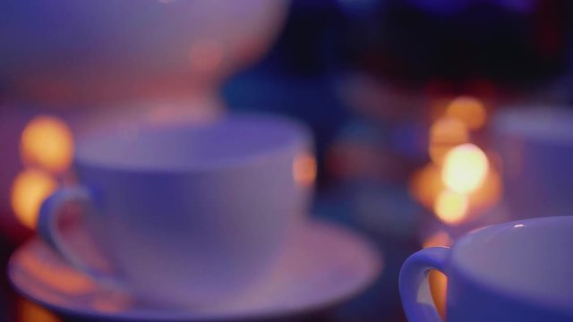 Focus shifting from teacup onto teapot with candle under it for heating on table in caffee