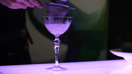 The process of making a cocktail, the barman in a beautiful glass on a long leg filters out the cocktail, a cocktail party, a contest of soft cocktails, a close-up video