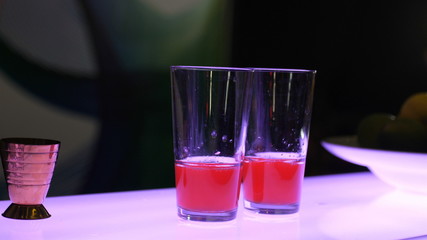 The process of making a cocktail, the bartender in two beautiful glasses, half full, squeezes the next ingredient, adds ice in large cubes and pours all the carbonated mineral water, non-alcoholic coc
