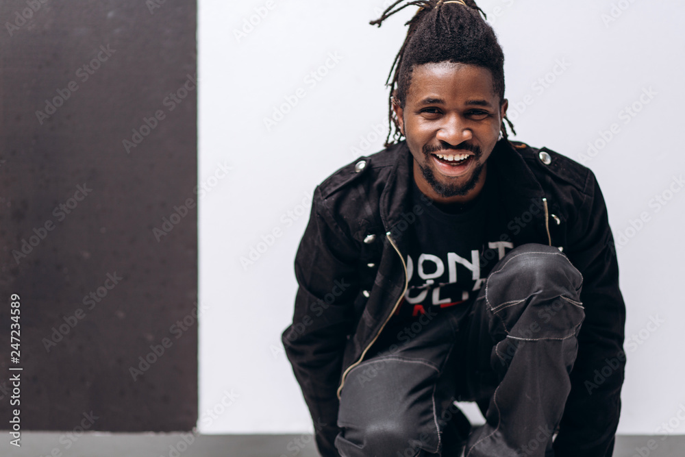 Wall mural one attractive smiling black man in black jacket and black pants over gray background