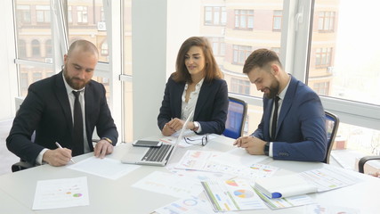 Office workers, employees of a large company, two young men, company executives and a woman are sitting at the table signing documents