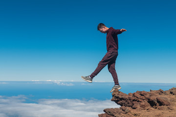 Obraz premium Extreme man standing and balancing on high mountain cliff edge
