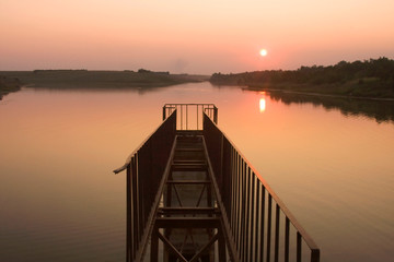 Fototapeta premium Sunset next to the water with broken bridge