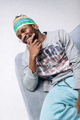 Portrait of a smiling black young model in a gray sweater and blue pants on a gray background near the chair