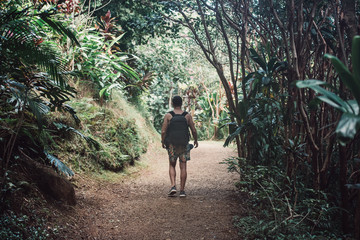 Tourist man with backpack walking on tropical jungle road