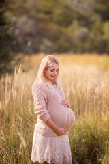 Fototapeta na wymiar Pretty young pregnant woman hugging her pregnant belly in park in beautiful sunny day. Family, motherhood, love, health, innocence and care