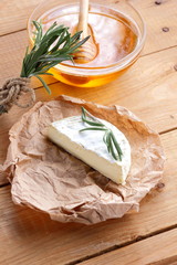 Camembert with rosemary branches on wooden boards. Soft cheese on parchment paper. Cheese with and honey on wooden background