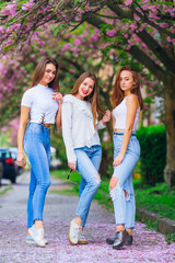 The girls smile standing on the sidewalk near the Japanese cherr