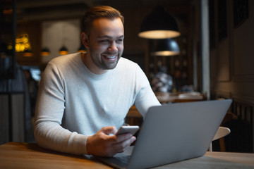 Young smiling businessman with laptop and smartphone on table.