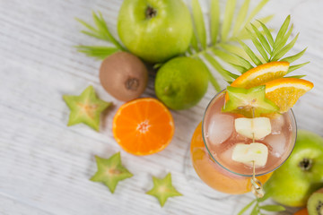 Summer cocktail with various tropical fruits around. Apple, kiwi, tangerine, orange, mango, carambola.