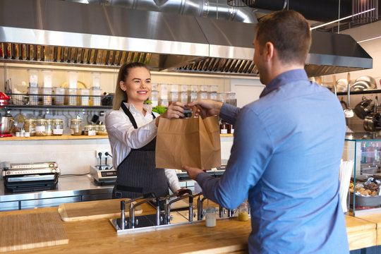 Waitress serving takeaway food to customer at counter in small family eatery restaurant. 