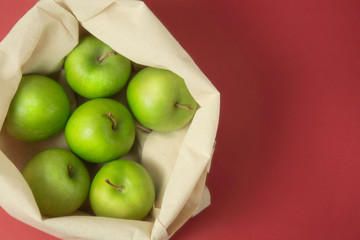 Bio fruit - green apples in white tote canvas fabric. Eco bag cloth shopping sack on colrful red background . Zero waste concept. Copy space.