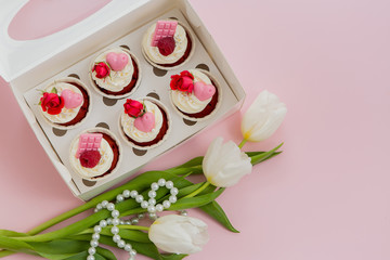gift box with cupcakes on pink background.Cupcakes decorated with pink cream, sugar flowers, beads, gold and macaroon with the words love in boxes with ribbons. On a white wooden table. Background lay