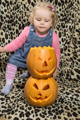 a little blonde girl is interested in two cut for halloween pumpkins