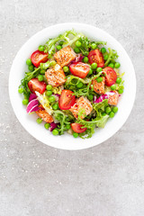 Healthy lunch vegetable salad with baked salmon fish, fresh green peas, lettuce and tomato. Top view