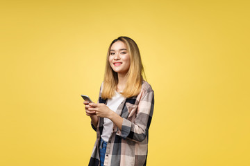 Image of satisfied asian woman with long hair smiling and texting on cell phone holding in hand isolated over yellow background