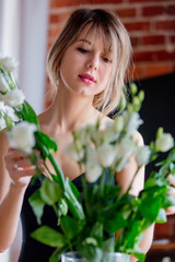 a girl dressed in a black dress is holding white roses in a bouquet before putting them in a vase. Sprint time concept
