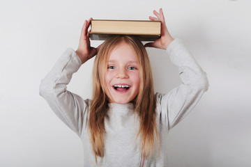 Portrait of little happy girl holding book on her head. Schoolgirl portrait, education concept. 