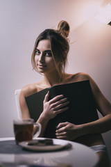 Woman sitting on chair covering chest with book near table with tea