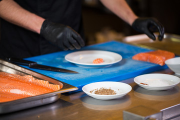 Fototapeta na wymiar Theme cooking is a profession of cooking. Close-up of a Caucasian man's hand in a restaurant kitchen preparing red fish fillets salmon meat in black latex gloves uniform