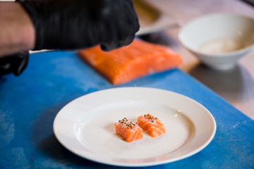 Theme cooking is a profession of cooking. Close-up of a Caucasian man's hand in a restaurant kitchen preparing red fish fillets salmon meat in black latex gloves uniform