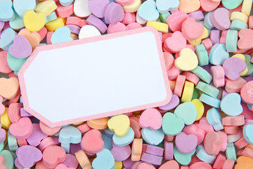 Brightly colored candy hearts, white card with pink border laying on top for copy space....