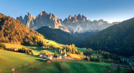 Landscape with village with houses, church, green meadows, trees, rocks, blue sky. Santa Maddalena...
