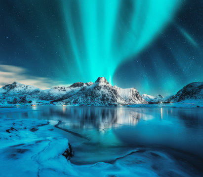 Aurora borealis over snowy mountains, frozen sea coast, reflection in water at night. Lofoten islands, Norway. Northern lights. Winter landscape with polar lights, ice in water. Starry sky with aurora © den-belitsky
