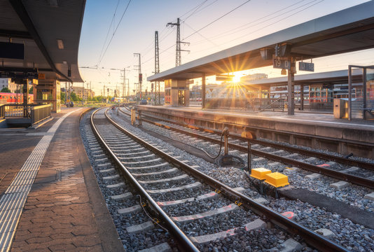 Railway station at sunset. Industrial landscape with railroad, railway platfform, buildings, blue sky with orange sunlight in the evening. Railway junction in summer in Europe. Transportation
