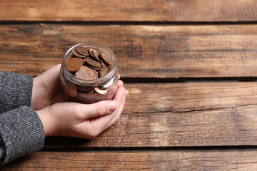 Woman holding donation jar with coins at wooden table, closeup. Space for text