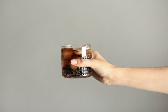 Woman holding glass of tasty refreshing cola with ice cubes on color background, closeup view