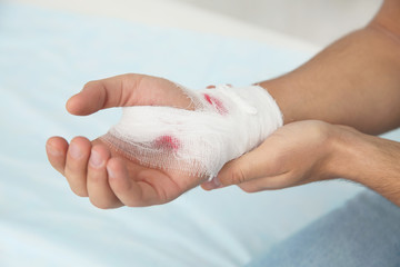 Young man with bandage on injured hand in clinic, closeup. First aid