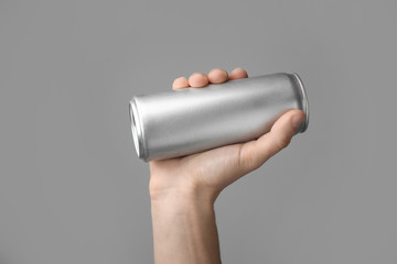 Man holding aluminum can with beverage on grey background, closeup. Space for design