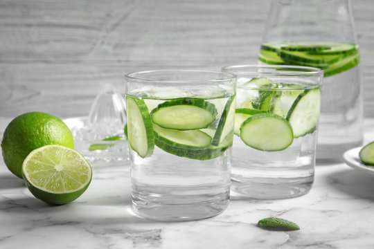Glasses with fresh cucumber water on table against light background
